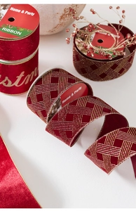 Close-up of red velvet Christmas ribbon with gold Merry Christmas lettering and grid patterns