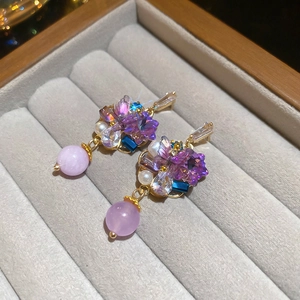 Detailed view of bohemian gold earrings with purple crystals and pearls in a velvet box