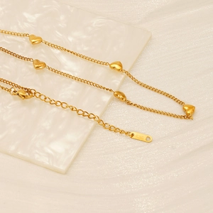 Collar de acero inoxidable chapado en oro de 18K con dijes de corazón sobre mármol blanco