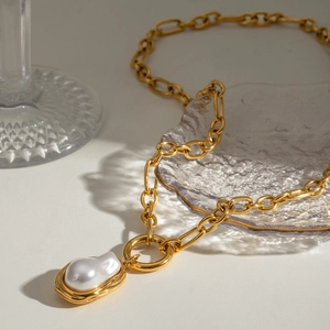 Elegant gold chain necklace featuring a baroque pearl pendant on a shell glass plate