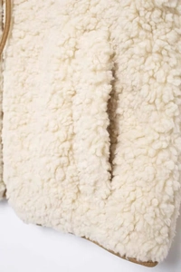 Detail of fleece vest pocket with brown piping on cream white sherpa fabric material