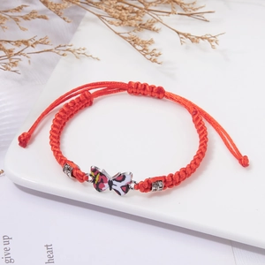 Handmade red string bracelet with colorful butterfly pendant and silver beads on ceramic tray