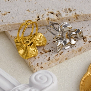 Artistic macro shot of gold and silver irregular pleated open rings on beige travertine