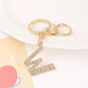 Macro shot of gold letter W keychain with rhinestones on a white ceramic tray
