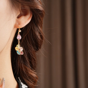 Detail of gold dangling earrings with pink teardrop stones and colorful bow design