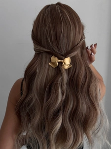 Detail view of a golden alloy bow hair clip worn on a half-up ponytail hairstyle