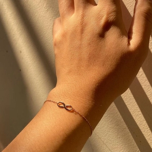 Minimalist rose gold infinity symbol bracelet on wrist with elegant shadow lighting