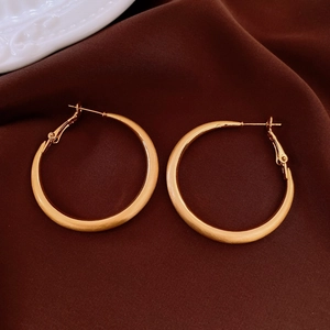 Dettaglio macro di orecchini a cerchio placcati oro 18k con texture metallica opaca