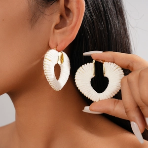 Close-up of white woven heart hoop earring with gold beaded trim on model ear