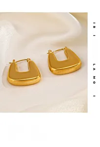 Détail de boucles d'oreilles carrées en acier doré 18 carats sur tissu de soie