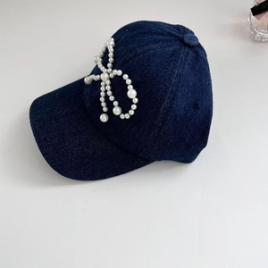Detailed view of hand-sewn pearl bow decoration on blue denim baseball cap for women
