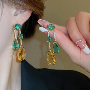 Détail de longues boucles d'oreilles dorées avec zircons verts et ambrés sur modèle