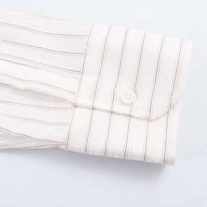 Detail of single-button cuff on white shirt with brown vertical stripes and fabric texture