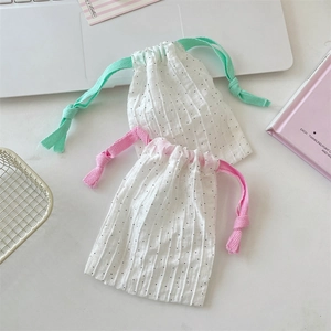 Polka dot drawstring bags in white with pink and green cords on a minimalist desk