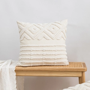 Modern creamy white bouclé embroidered cushion cover on a wooden bench with textured throw
