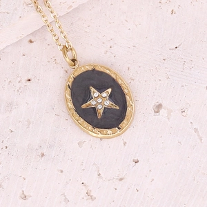 Macro shot of gold star necklace pendant with black enamel and sparkling zircon detail