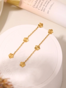Macro shot of 18K gold-plated clover tassel earrings next to luxury cosmetics