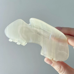 Close-up of a hand holding a polished light green jade guasha tool with natural texture