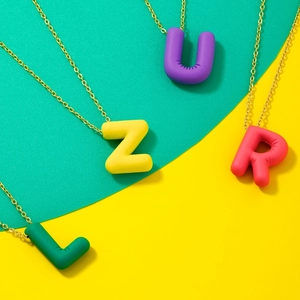 Detail of colorful matte letter pendants in green, yellow, purple and red with gold chains