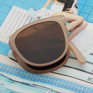 Foldable UV400 sunglasses in a brown frame showing compact storage design on a blue magazine