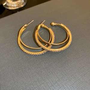 Close-up of gold double hoop earrings with crystal pavé on dark textured background