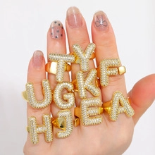 Close-up of gold-plated rings featuring white rhinestones in various initial letters