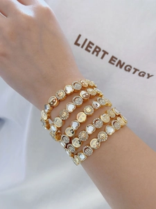 Detail of gold-plated bracelets featuring crystal-studded smiley face and sunflower charms