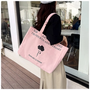Pink canvas tote bag with black floral print shown on shoulder in a street style view