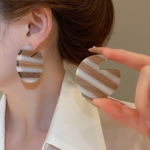 Detail showing retro C-shaped wood and resin geometric earrings on a model's ear