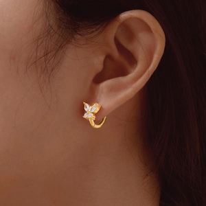 Close-up of a gold butterfly hoop earring with clear stones worn on a person's ear
