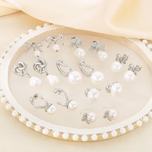 Flat lay of vintage silver bow and pearl earrings set on an elegant beige satin background