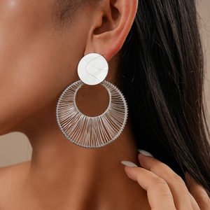 Close-up of silver hollow woven circular earrings worn by a model in soft light