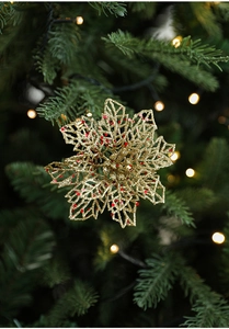 Gros plan d'une fleur évidée dorée avec paillettes rouges sur branche de sapin de Noël