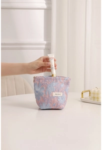 Pink jacquard cosmetic bag with blue floral embroidery showing hand cream storage capacity