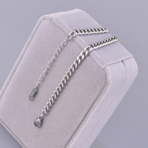 Macro detail of silver stainless steel Cuban link chain with lobster clasp and K18 tag