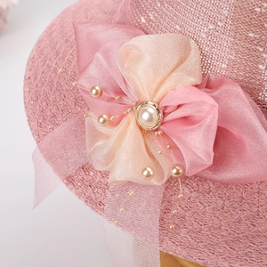 Dettaglio di un cappello da sole intrecciato rosa con fiocco di seta, perle e decori eleganti