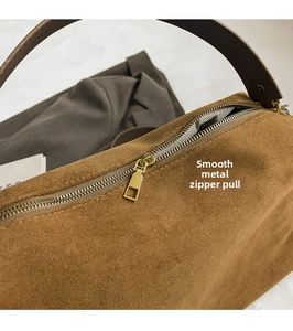 Detail of the golden metal zipper closure on the brown suede baguette shoulder bag