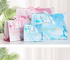 Detailed view of pink and blue marble gift bags with elegant ribbon handles and gold text