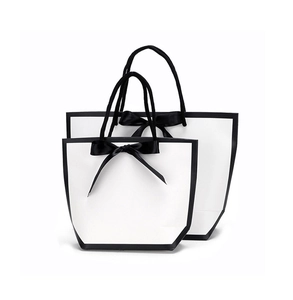 Detailed view of white trapezoid paper gift bags with black trim and elegant ribbon bows