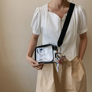 Detail view of transparent PVC crossbody bag with wide black strap and floral silk scarf