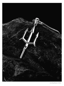 Detailed close-up of a silver Neptune trident pendant resting on a dark natural stone