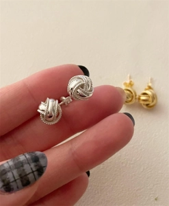 Detalle macro de pendientes de nudo en plata esterlina S925 sostenidos a mano, plata y oro