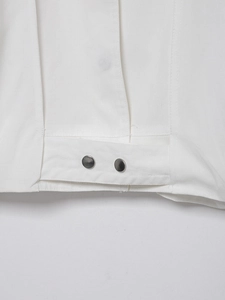 Detailed close-up of white linen bomber jacket showing silver metal snaps and stitching