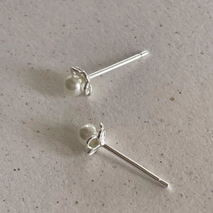 Close-up of minimalist silver pearl stud earrings on a textured grey background surface