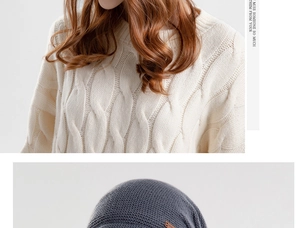 Detail van crème kabeltrui en donkergrijze beanie met bruine lederen patch label erop