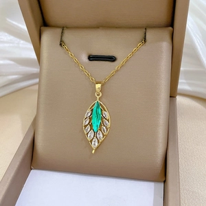 Detailed close-up of a gold leaf pendant with a green gemstone and white zircons