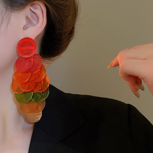 Detailed view of layered colorful circular shell tassel earrings worn by a model