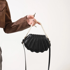 Detail of shell-shaped crossbody bag with elegant pearl handle and black leather finish