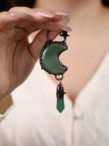 Detail of crescent moon necklace with green stone and star charms on bronze sweater chain