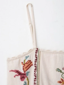 Detailed shot of beige camisole featuring colorful floral embroidery and scalloped edges